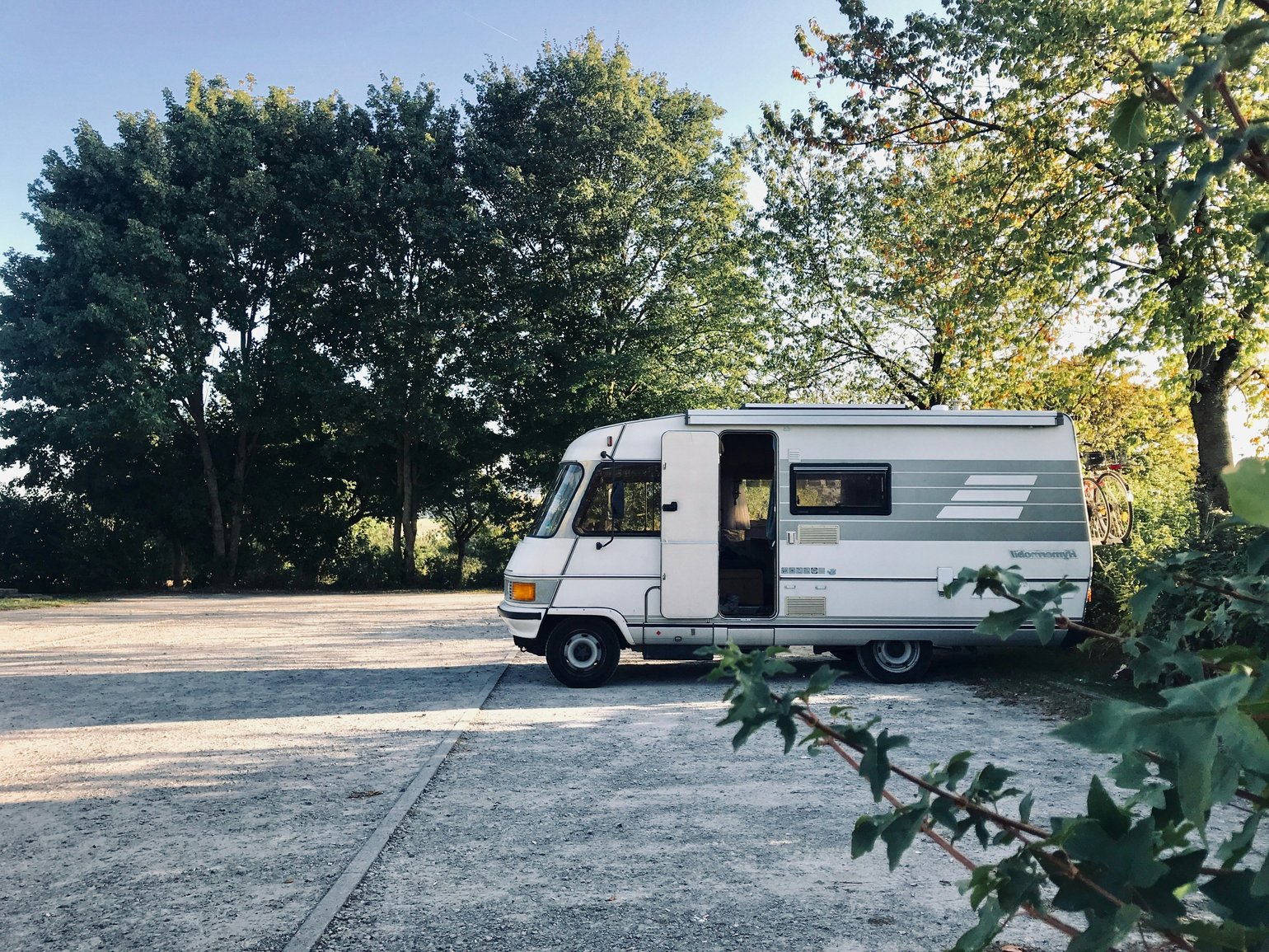 Ein Wohnmobil steht im Sonneaufgang auf einem befestigten Parkplatz in der Natur