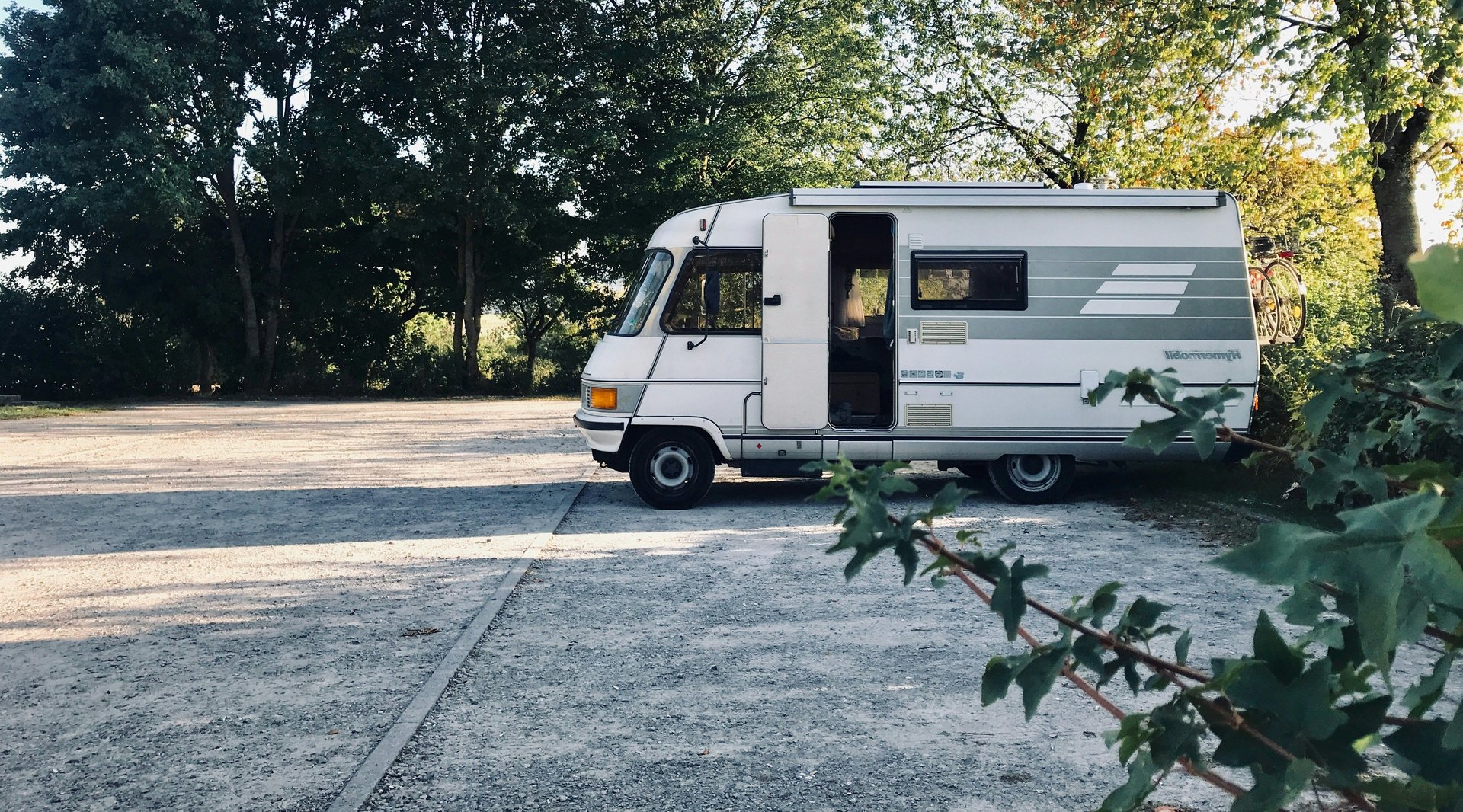 Ein Wohnmobil steht im Sonneaufgang auf einem befestigten Parkplatz in der Natur
