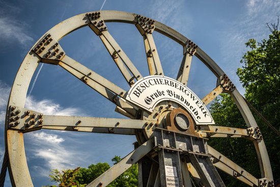 Ein großes Förderrad vor blauem Himmel trägt das Schild des Besucherbergwerks Grube Bindweide