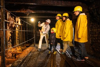 Besucher erleben die Gästeführung unter Tage mit gelbem Helm und Regenjacke
