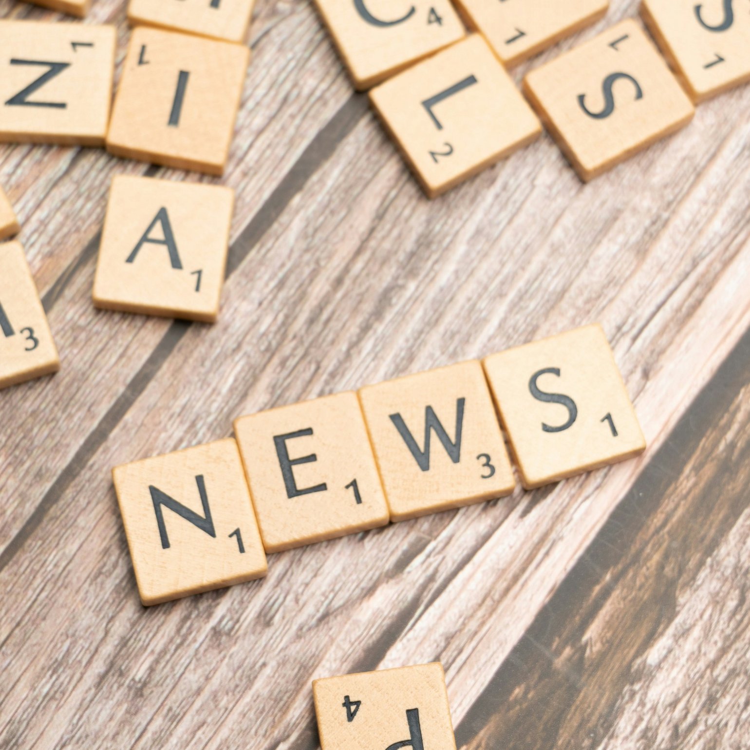 Buchstabenplättchen liegen durcheinander auf dem Tisch: Es ist das Wort "News" zu lesen. 