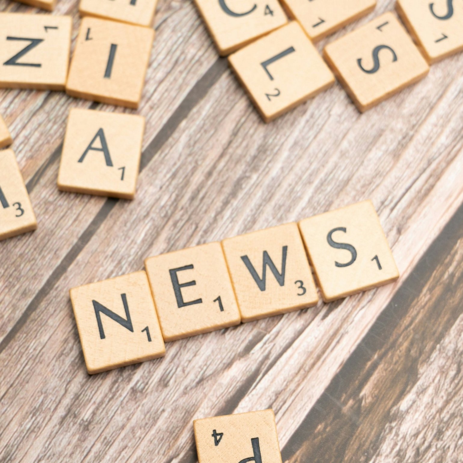 Buchstabenplättchen liegen durcheinander auf dem Tisch: Es ist das Wort "News" zu lesen. 