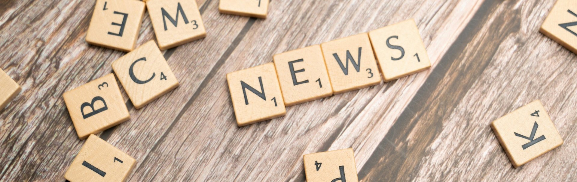 Buchstabenplättchen liegen durcheinander auf dem Tisch: Es ist das Wort "News" zu lesen. 