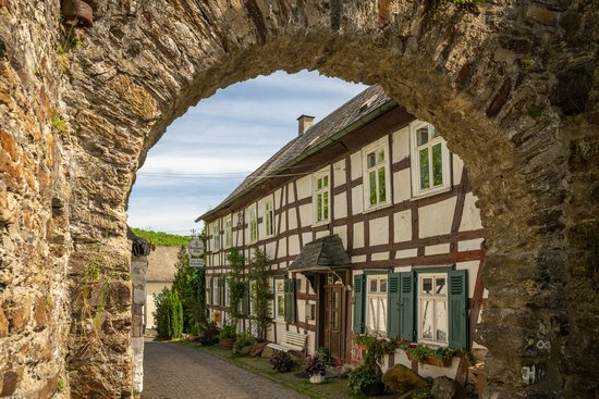 Durch ein Tor in einer Bruchsteinmauer schaut man auf ein altes Fachwerkhaus in Freusburg