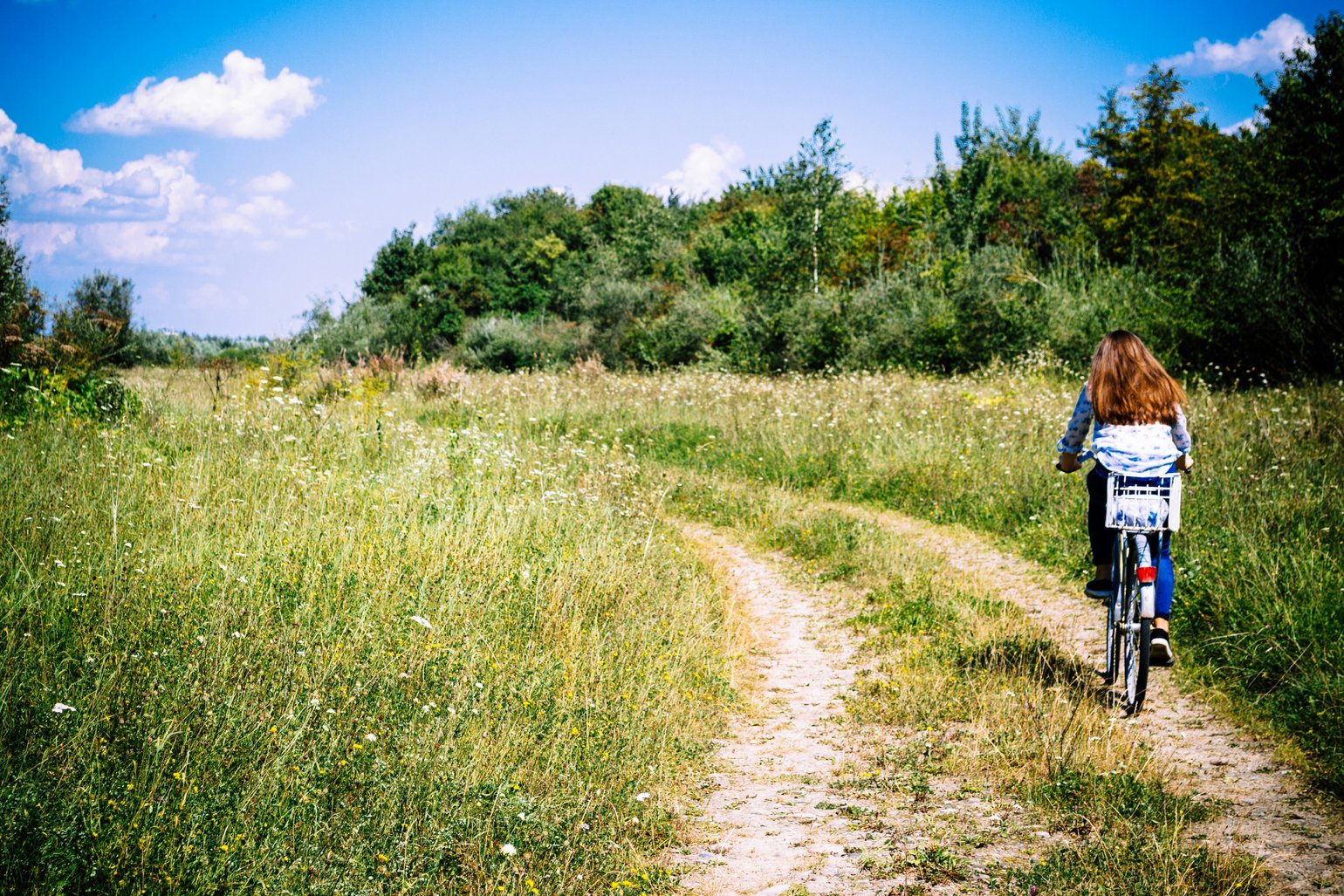Eine Frau von hinten radelt über einen Feldweg.