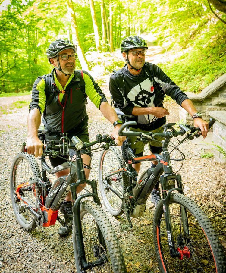 Zwei Radfahrer stehen mit den Mountain-Bikes im sonnigen Wald.