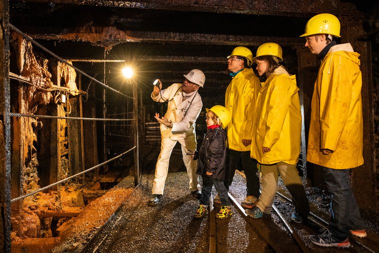 Eine Familie besucht das Besucherbergwerk Grube Bindweide unter Tage und lässt sich von dem Grubenführer etwas erklären