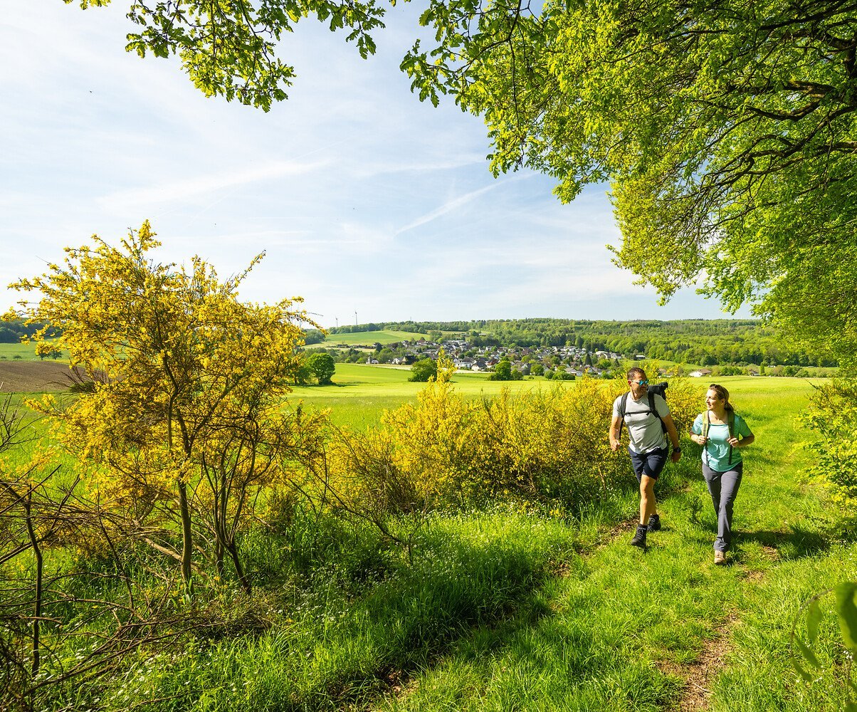 Zwei Wanderer auf einem Waldweg im Frühling vor einer Ortschaft