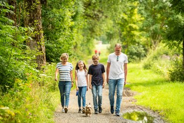 Eine Familie mit Kindern und Hund geht einen Weg entlang.