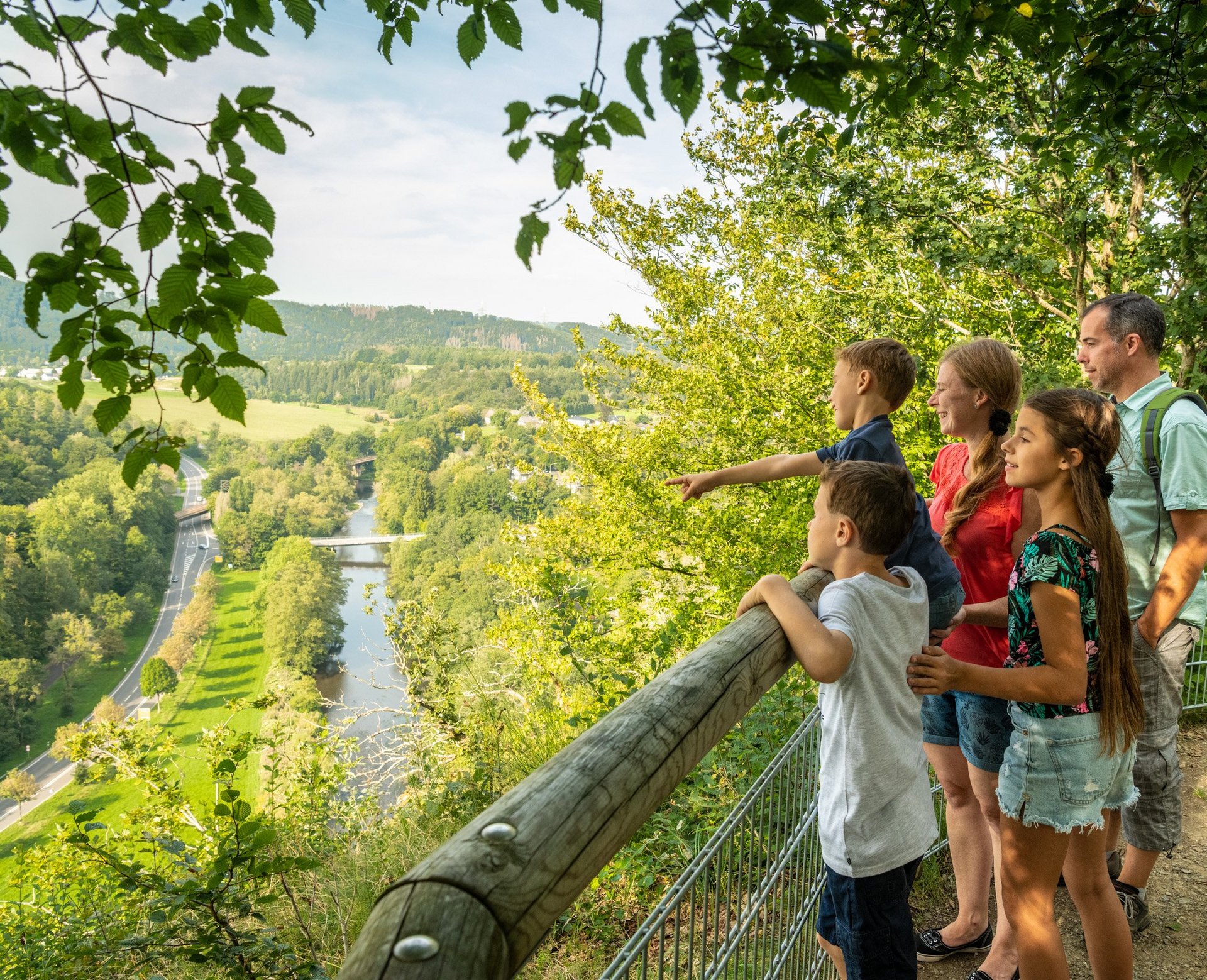 Eine Familie schaut von einem Aussichtspunkt in das sonnige Siegtal