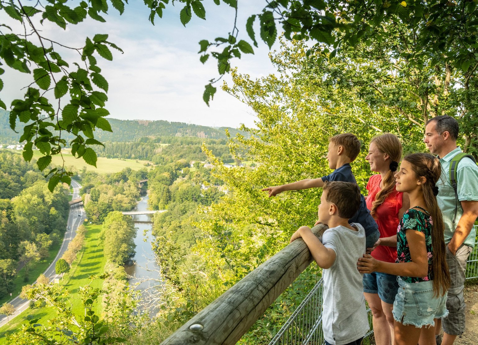 Eine Familie schaut von einem Aussichtspunkt in das sonnige Siegtal