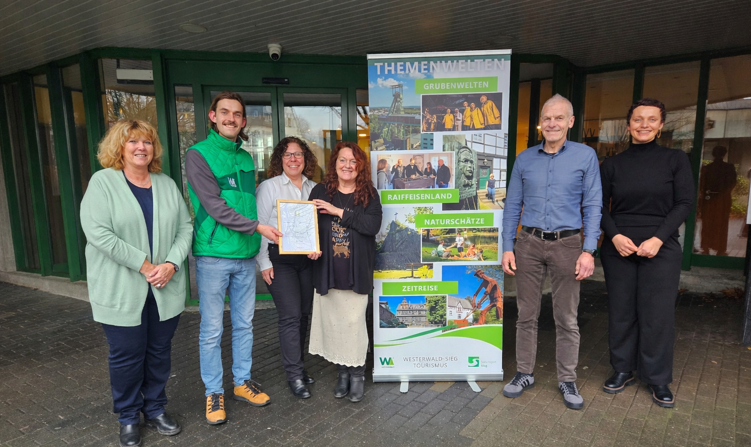 Gruppenfoto vor Banner der Themenwelten mit einer Zertifikatübergabe