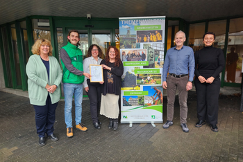 Gruppenfoto vor Banner der Themenwelten mit einer Zertifikatübergabe