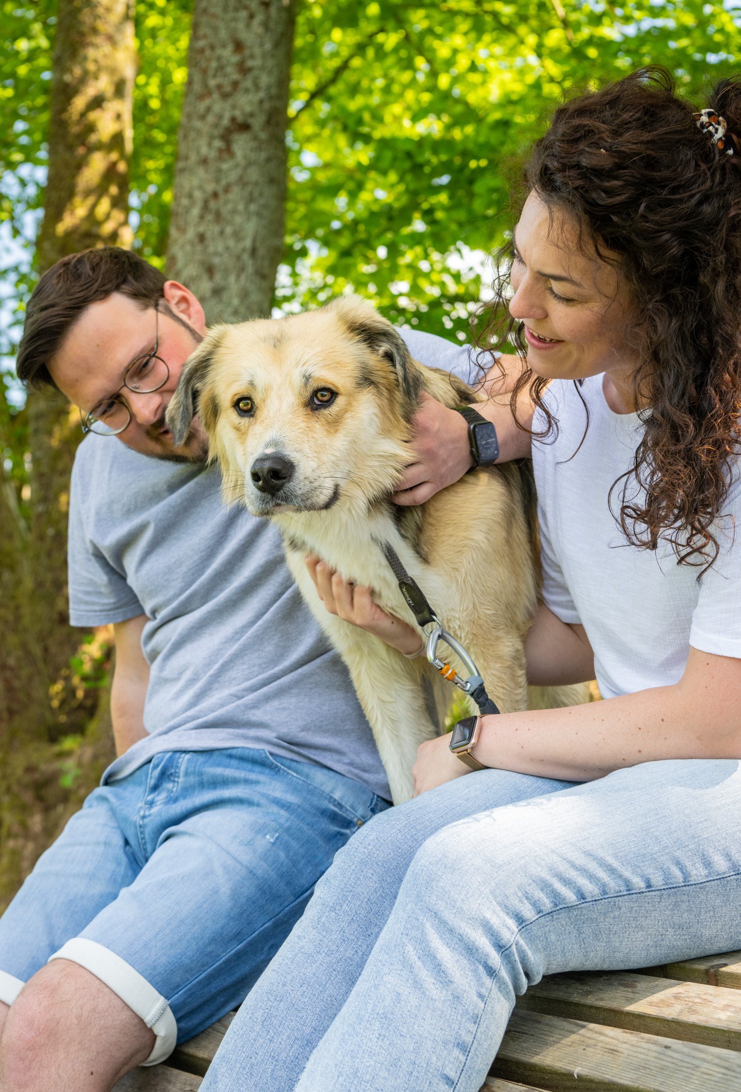 Ein Paar kuschelt bei einer Wanderpause auf der Bank mit einem Hund.