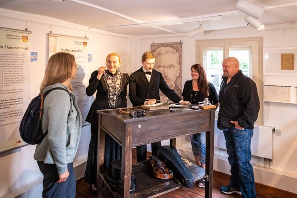 Im Raiffeisenhaus Hamm besucht eine Gruppe die Wachsfigur von Friedrich Wilhelm Raiffeisen und die Gästeführerin gewandet in den Kleidern aus der Zeit.