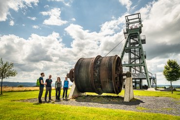 Eine Gruppe Wanderer steht an der riesigen Förderspule des Barbaraturms auf dem Malberg