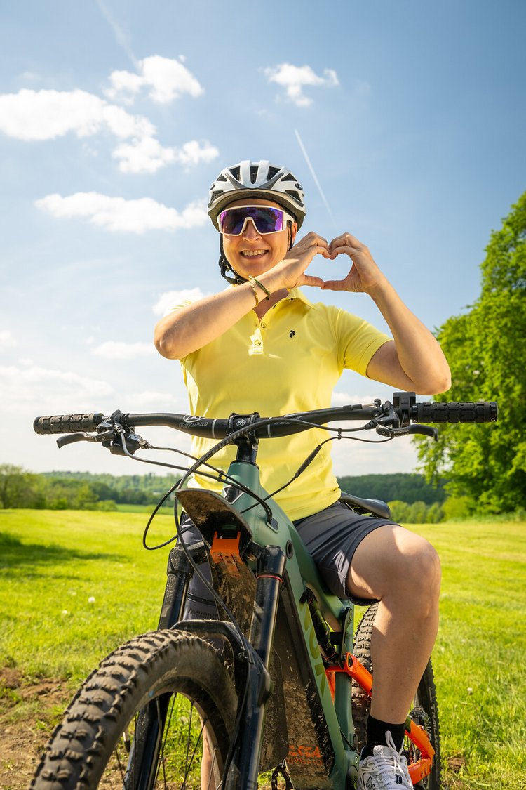 Fahrradfahrerin auf einem E-Bike formt mit den Händen ein Herz in der Luft