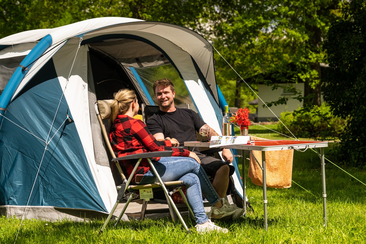 Ein Paar sitzt auf Campingstühlen vor einem Zelt in der Sonne