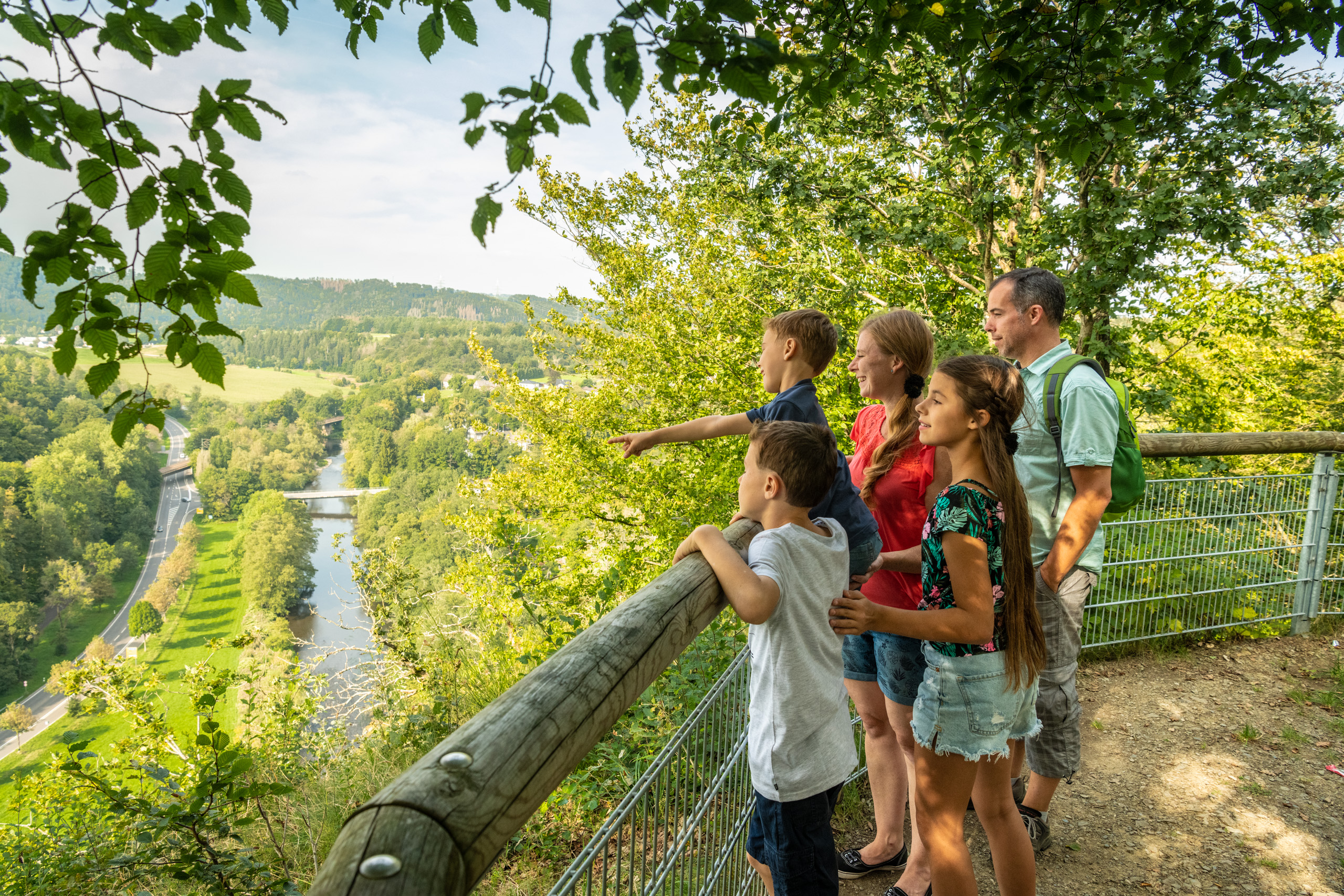 Eine Familie schaut von einem Aussichtspunkt in das sonnige Siegtal