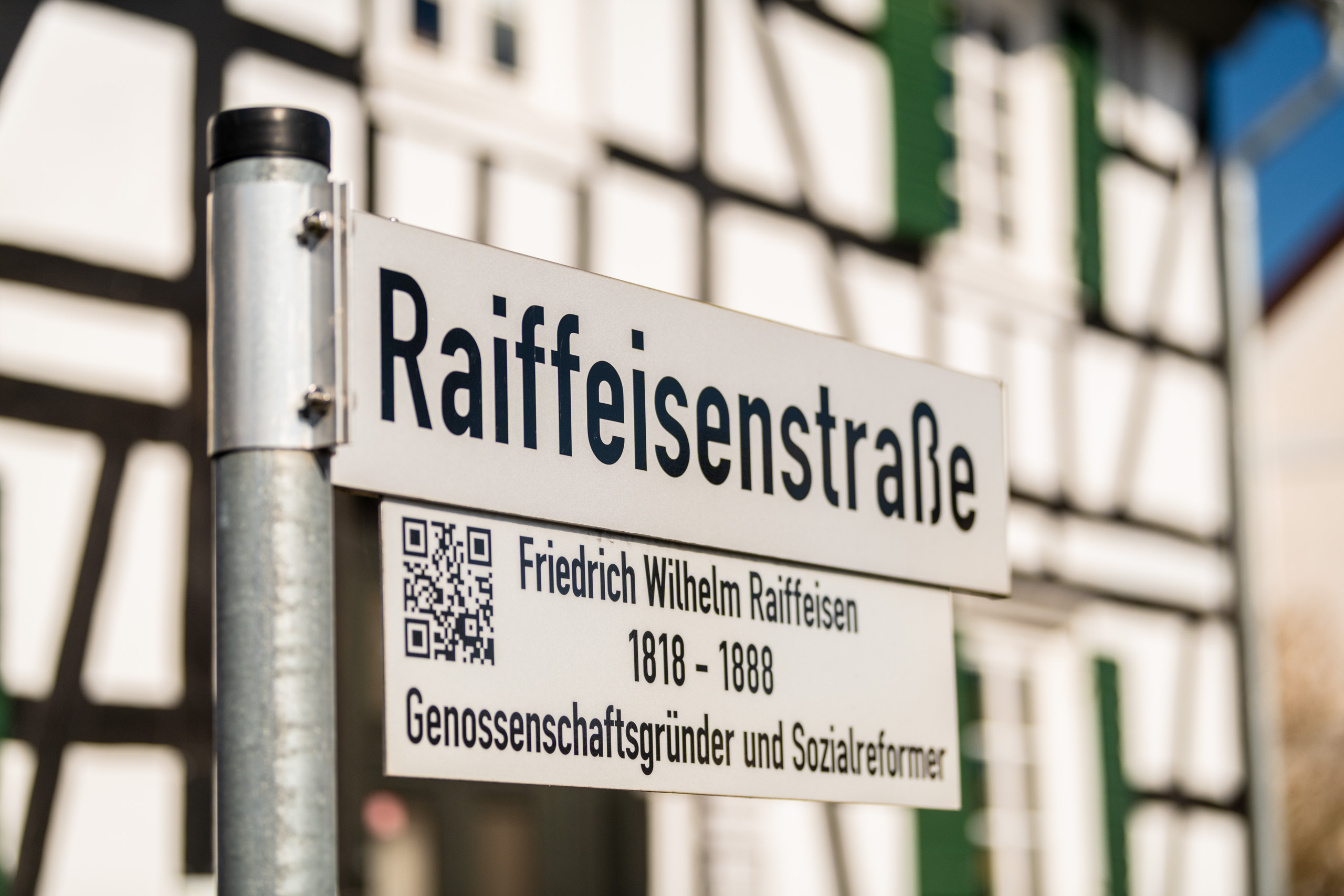 Ein Straßenschild "Raiffeisenstraße" vor einem Fachwerkhaus, darunter eine Schild mit Informationen zu Friedrich Wilhelm Raiffeisen